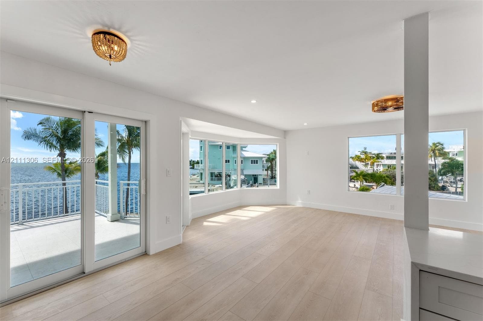 Light-filled interior featuring expansive wood-finish flooring, a bay window, sliding glass doors to a balcony, and decorative circular flush-mount lighting fixtures