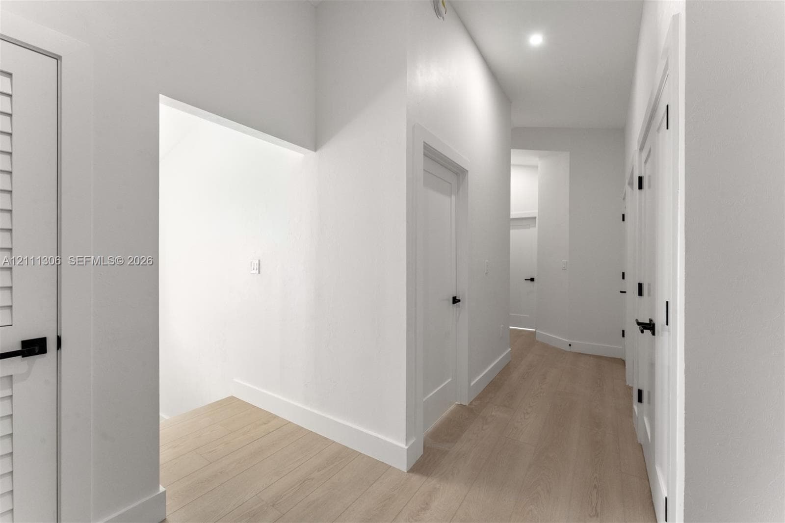 Hallway featuring wood-finish flooring, shaker-style interior doors, matte black hardware, and recessed lighting