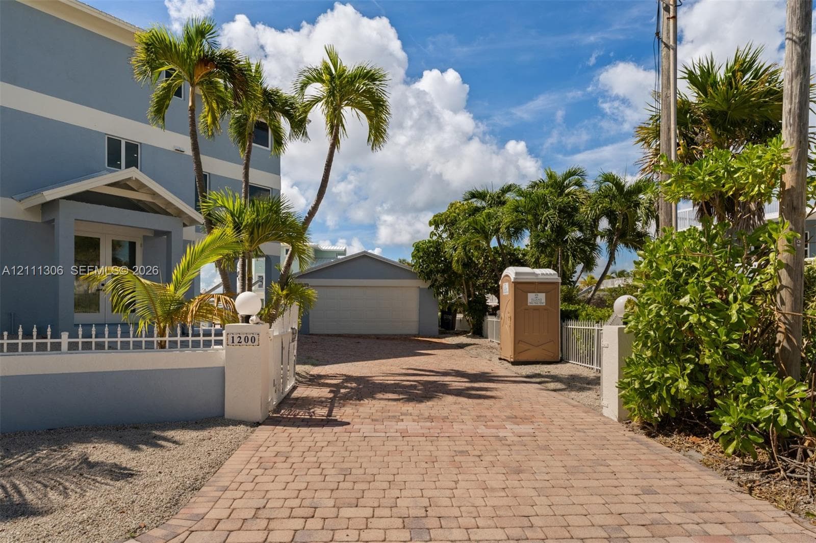 Multi-story residence featuring a paved brick driveway, detached garage, and perimeter masonry wall with white metal fencing