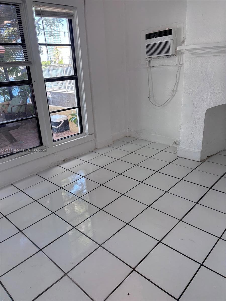 Glossy white ceramic tile flooring, multi-pane window with dark frames, wall-mounted air conditioning unit, and textured white wall finish