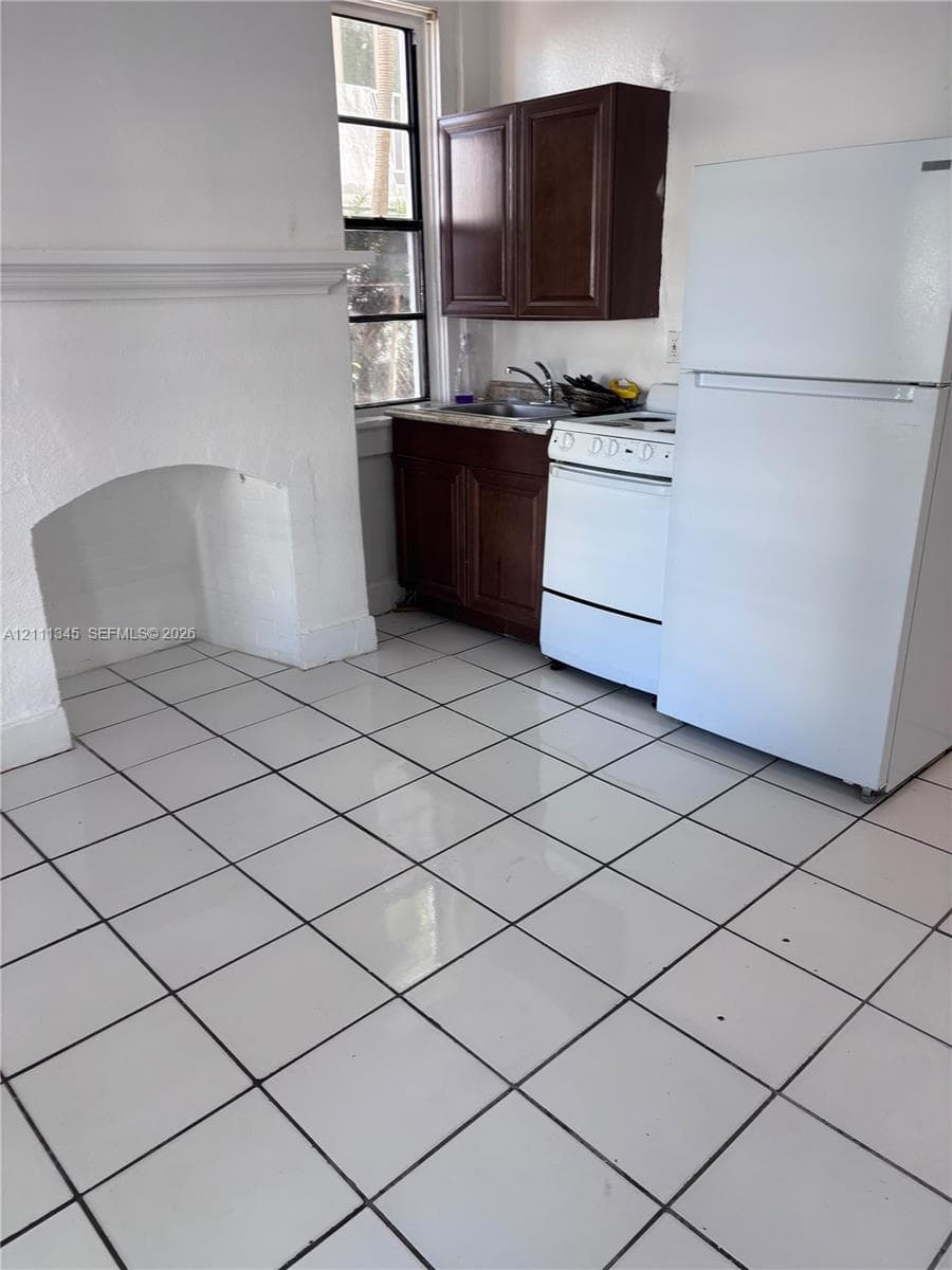 Kitchen featuring white ceramic tile flooring, dark wood-finish cabinetry, a built-in white stove, and a decorative fireplace mantel
