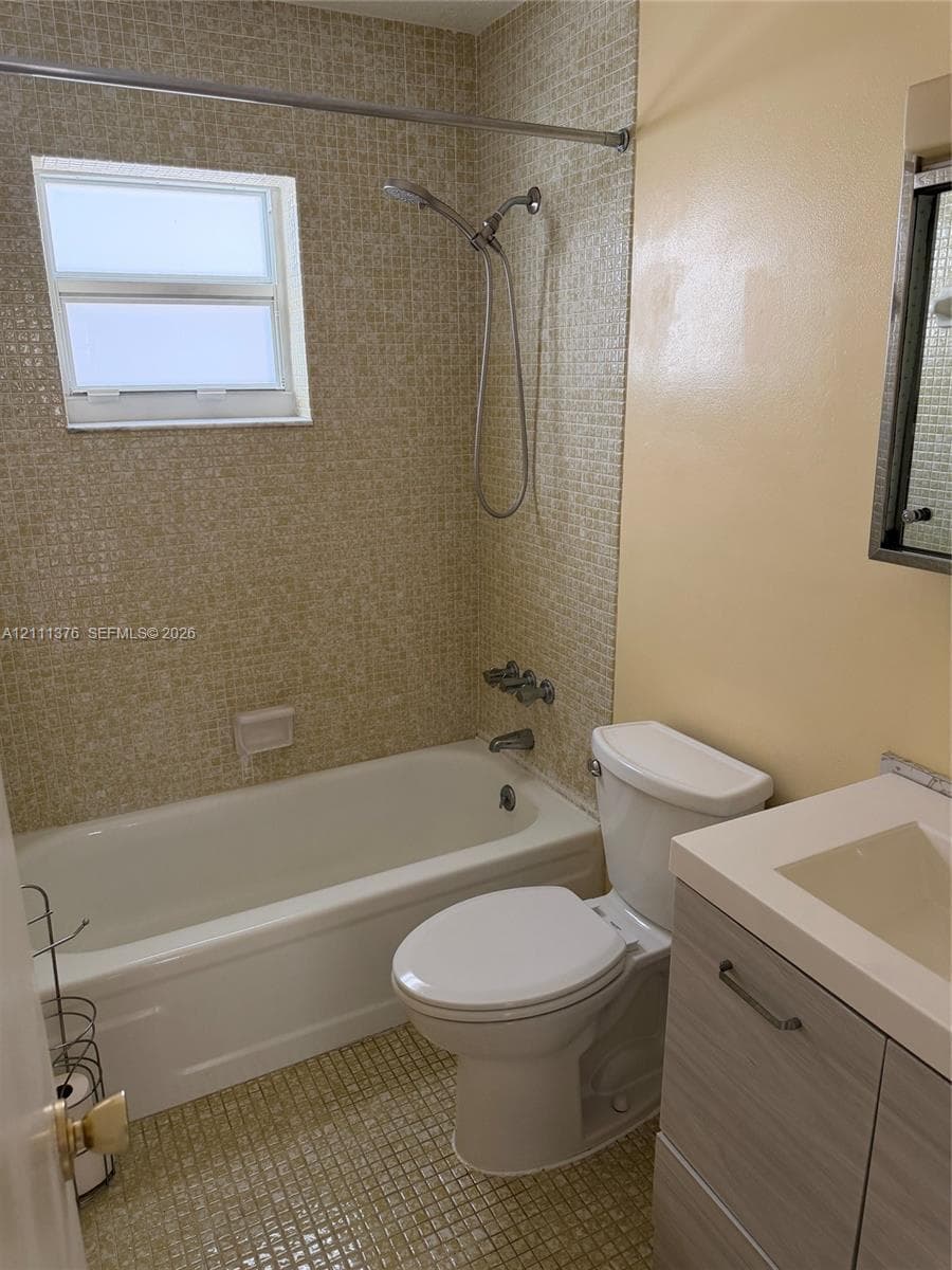 Bathroom featuring mosaic tile wall accents, a built-in bathtub with shower head, a wood-finish vanity with an integrated basin, and an inset window