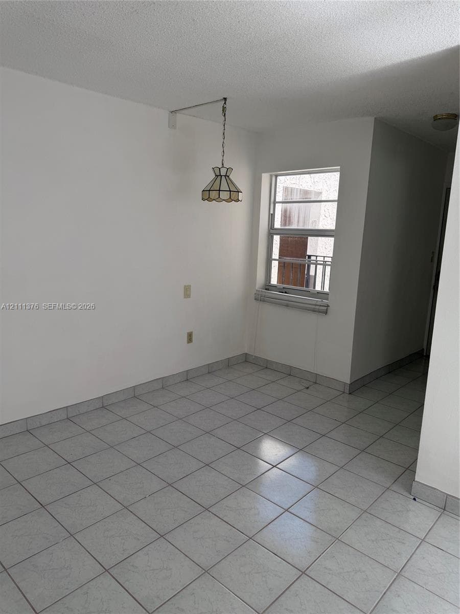 Neutral-toned tile flooring, white wall finish, single-hung window with metal framing, and a decorative hanging pendant light fixture