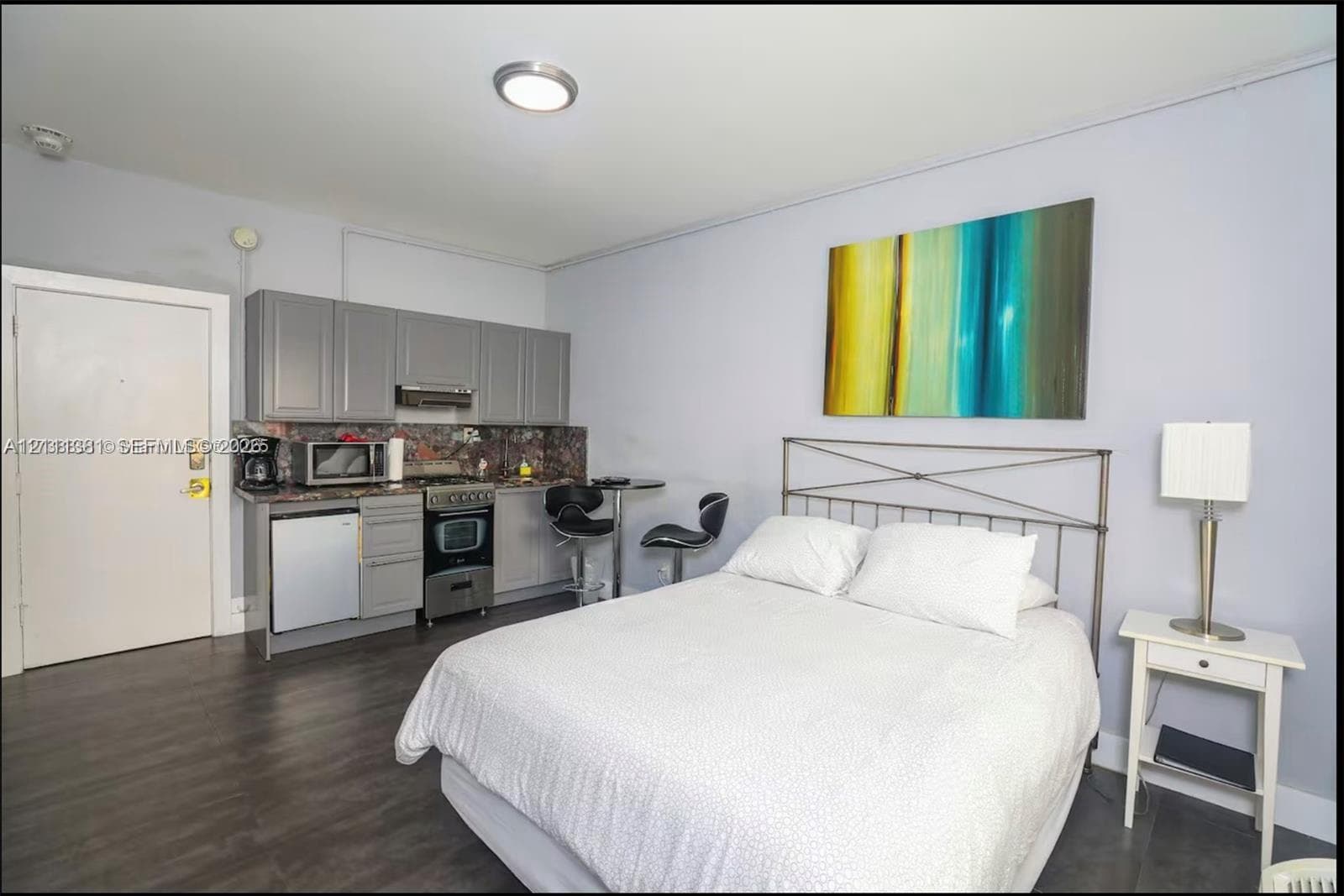 Kitchenette featuring grey cabinetry, dark stone-finish countertops, stainless steel appliances, and wood-finish flooring