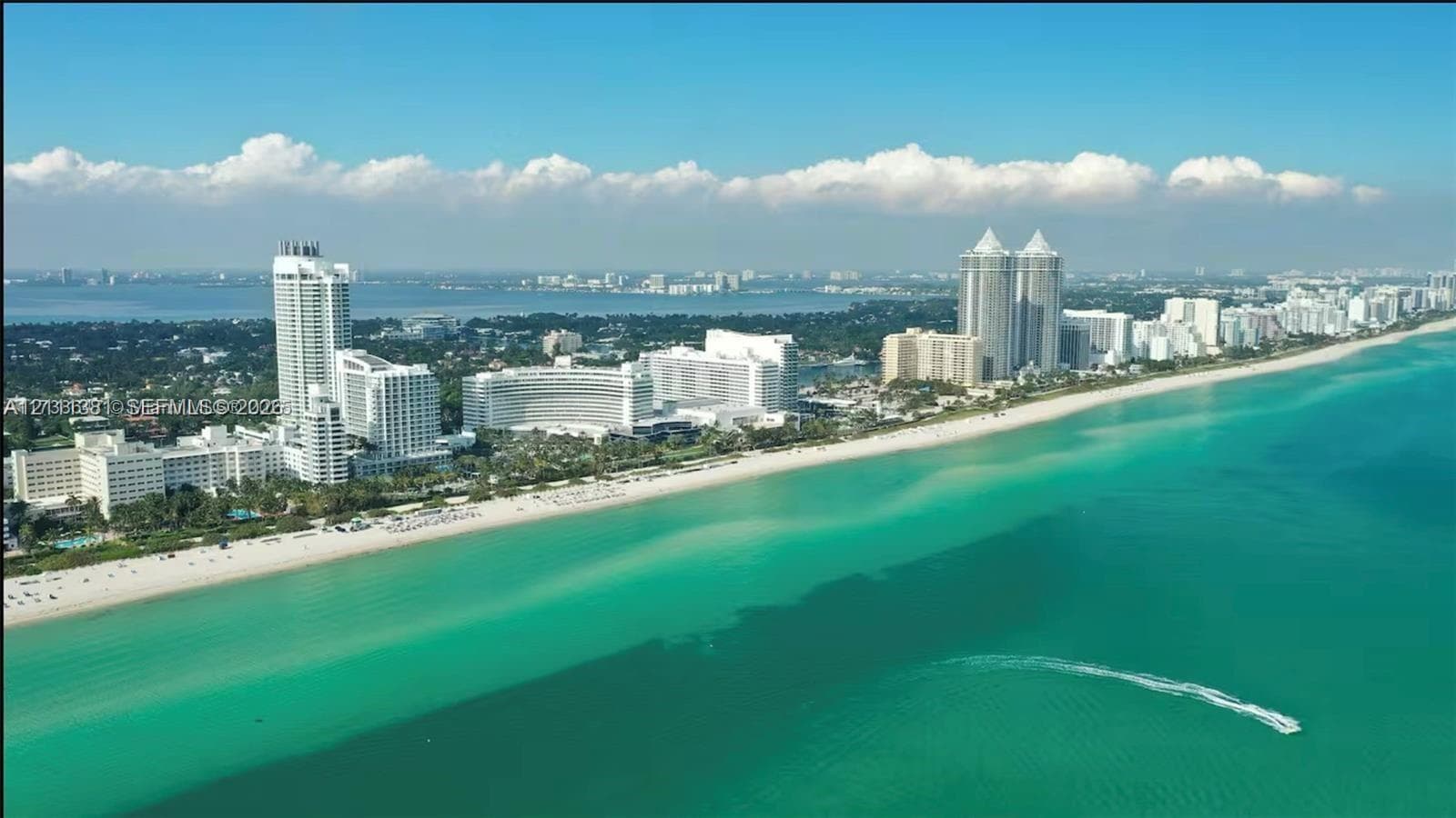 Aerial perspective of an expansive coastline featuring turquoise water, a sandy beach, and high-rise developments