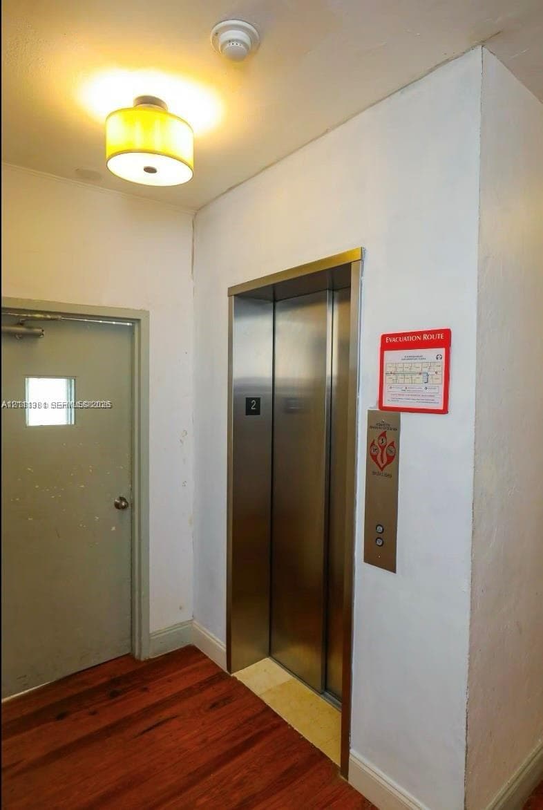 Elevator access with stainless steel doors, drum-style ceiling light fixture, and wood-finish flooring
