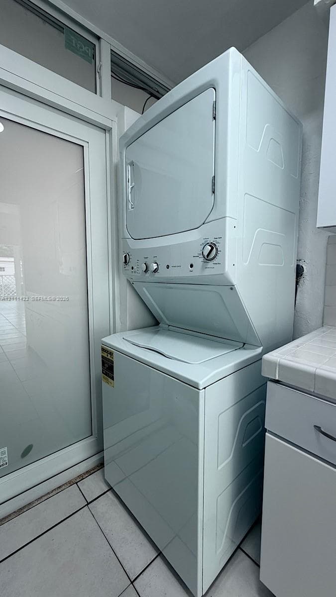 Stacked laundry unit with white finish, integrated cabinetry with tiled countertop, and glass-paneled exterior door