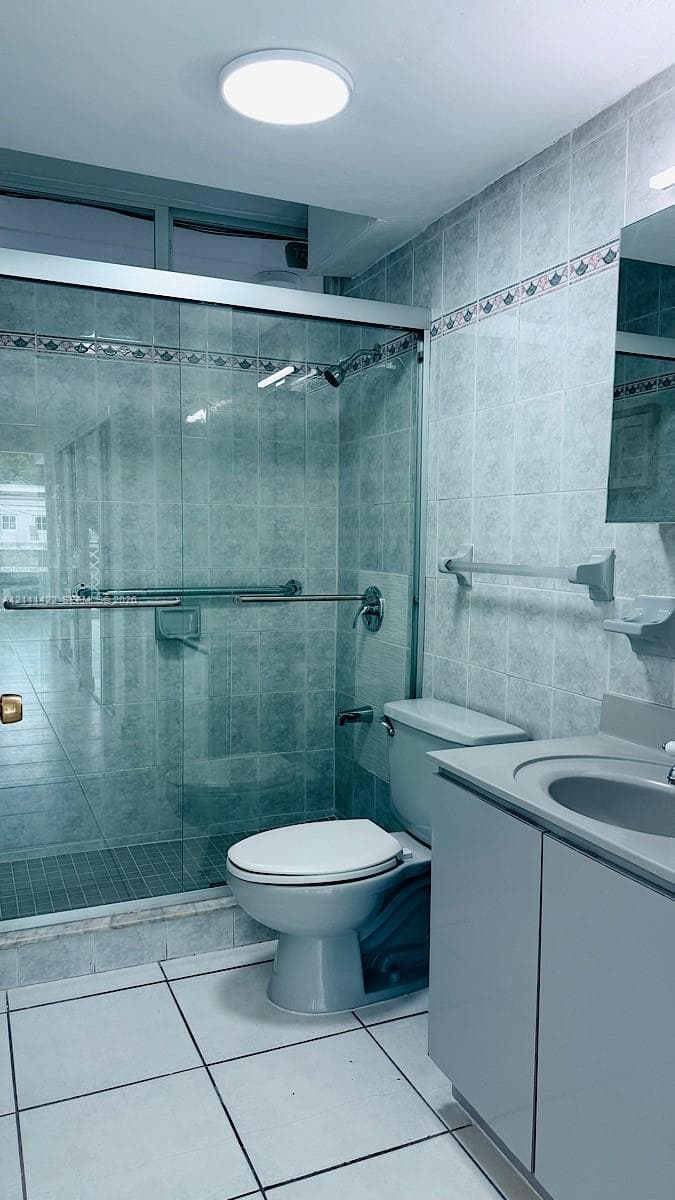 Bathroom featuring ceramic tile flooring, walk-in shower with sliding glass enclosure, vanity with integrated basin, flush-mount lighting, and wall-mounted metal hardware
