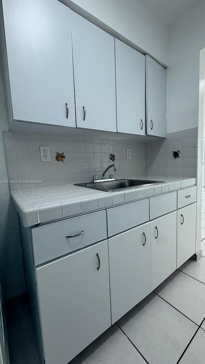 White cabinetry featuring metal pulls, square-tile countertop, integrated stainless steel sink, and decorative tile backsplash