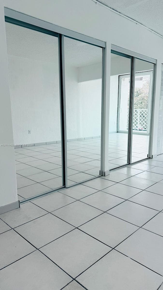 Floor-to-ceiling mirror-paneled sliding closet doors with metallic trim and neutral ceramic tile flooring