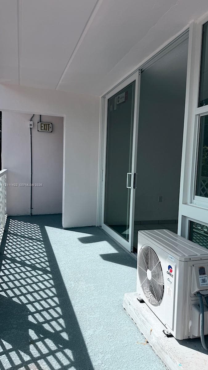 Covered balcony featuring a white metal railing, large sliding glass door, and a wall-mounted exterior HVAC unit