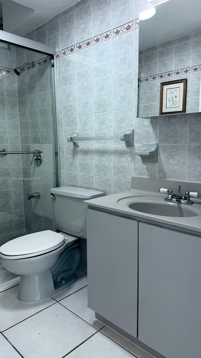 Bathroom featuring a grey vanity with an integrated basin, glass-enclosed shower, wall-mounted soap dish, metal towel bar, and floor-to-ceiling tilework with a decorative border