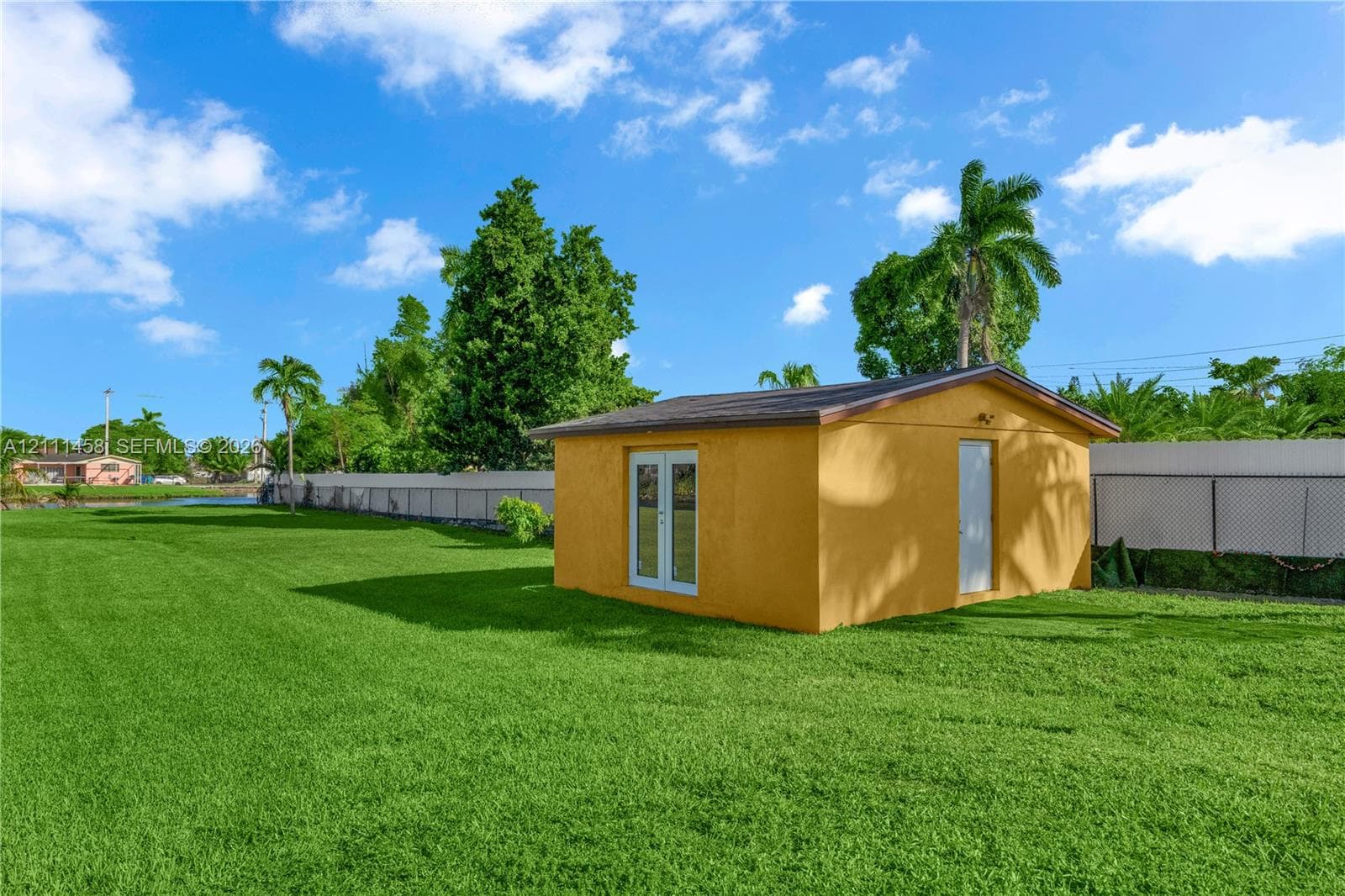 Expansive backyard featuring a manicured lawn, a detached outbuilding, French doors, and perimeter fencing