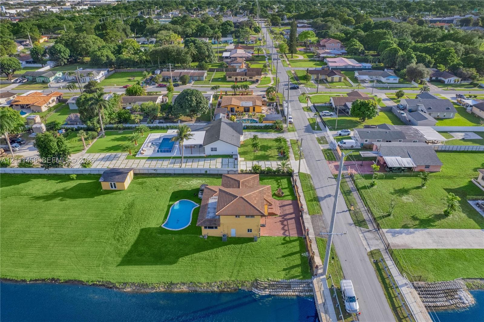 Aerial perspective featuring a waterfront property with an inground pool, expansive lawn, detached storage structure, and paved driveway