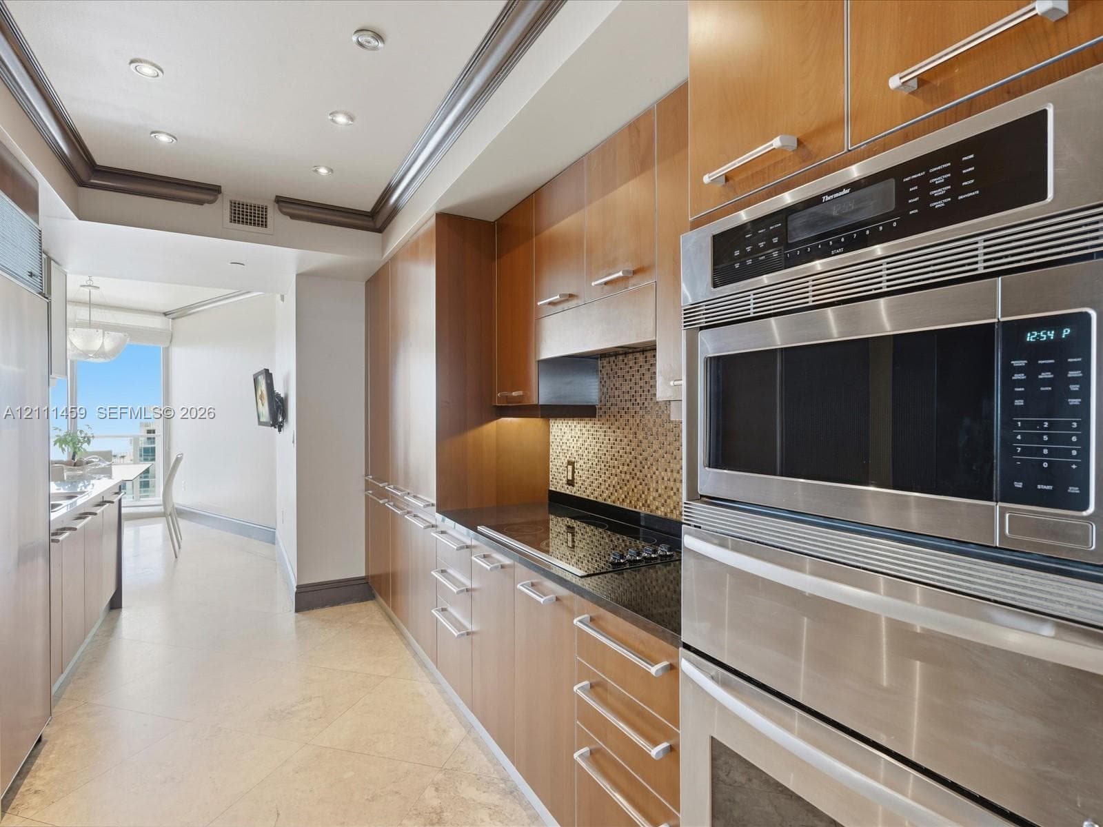 Kitchen featuring flat-panel wood cabinetry, integrated stainless steel double wall ovens, a glass cooktop, dark stone countertops, and stone tile flooring