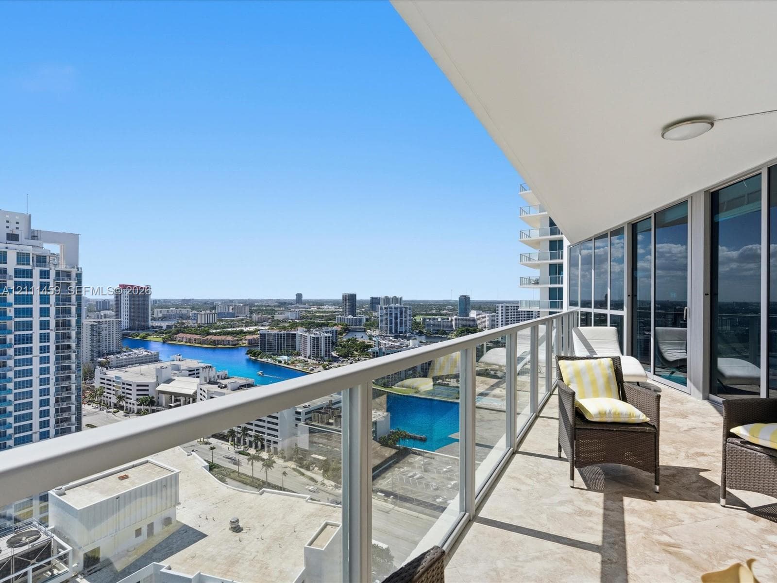 Private balcony featuring stone tile flooring, a glass-panel railing, and an overhead lighting fixture