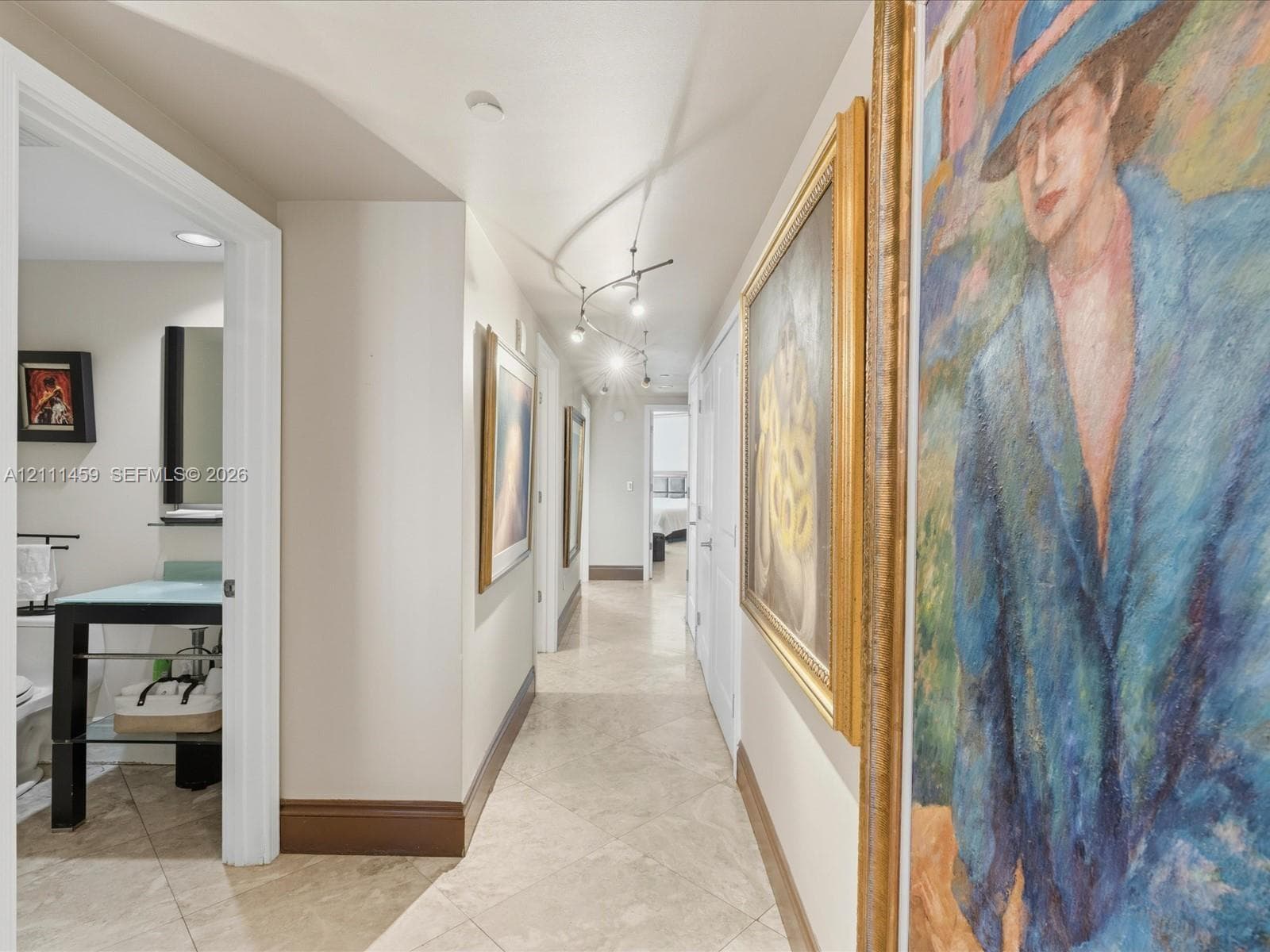 Hallway featuring diagonal-set stone tile flooring, directional track lighting, and a bathroom equipped with a glass-top console vanity