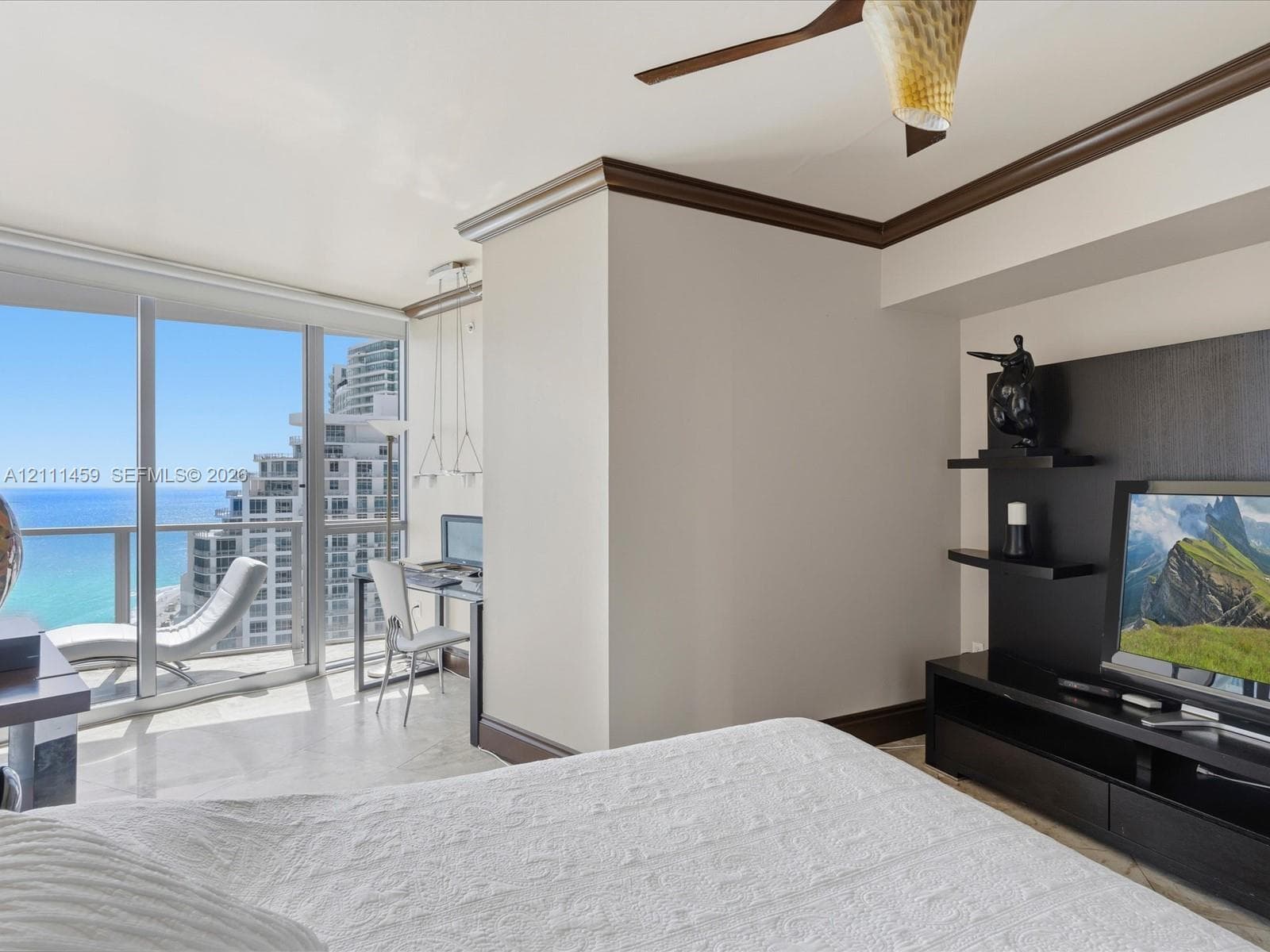 Floor-to-ceiling glass panel windows, built-in media console with tiered shelving, ceiling fan, crown molding, and polished stone flooring