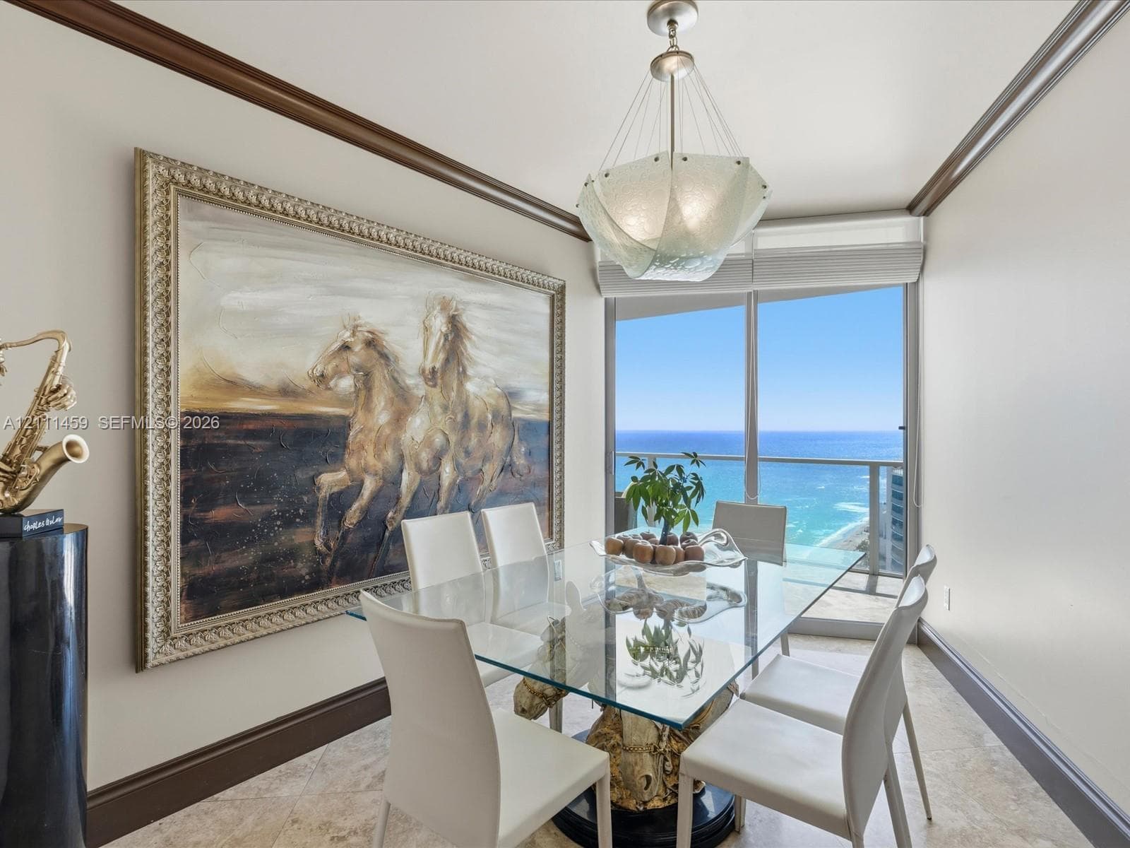 Dining space featuring stone tile flooring, crown molding, a custom pendant light fixture, and a floor-to-ceiling glass door opening to an oceanfront balcony