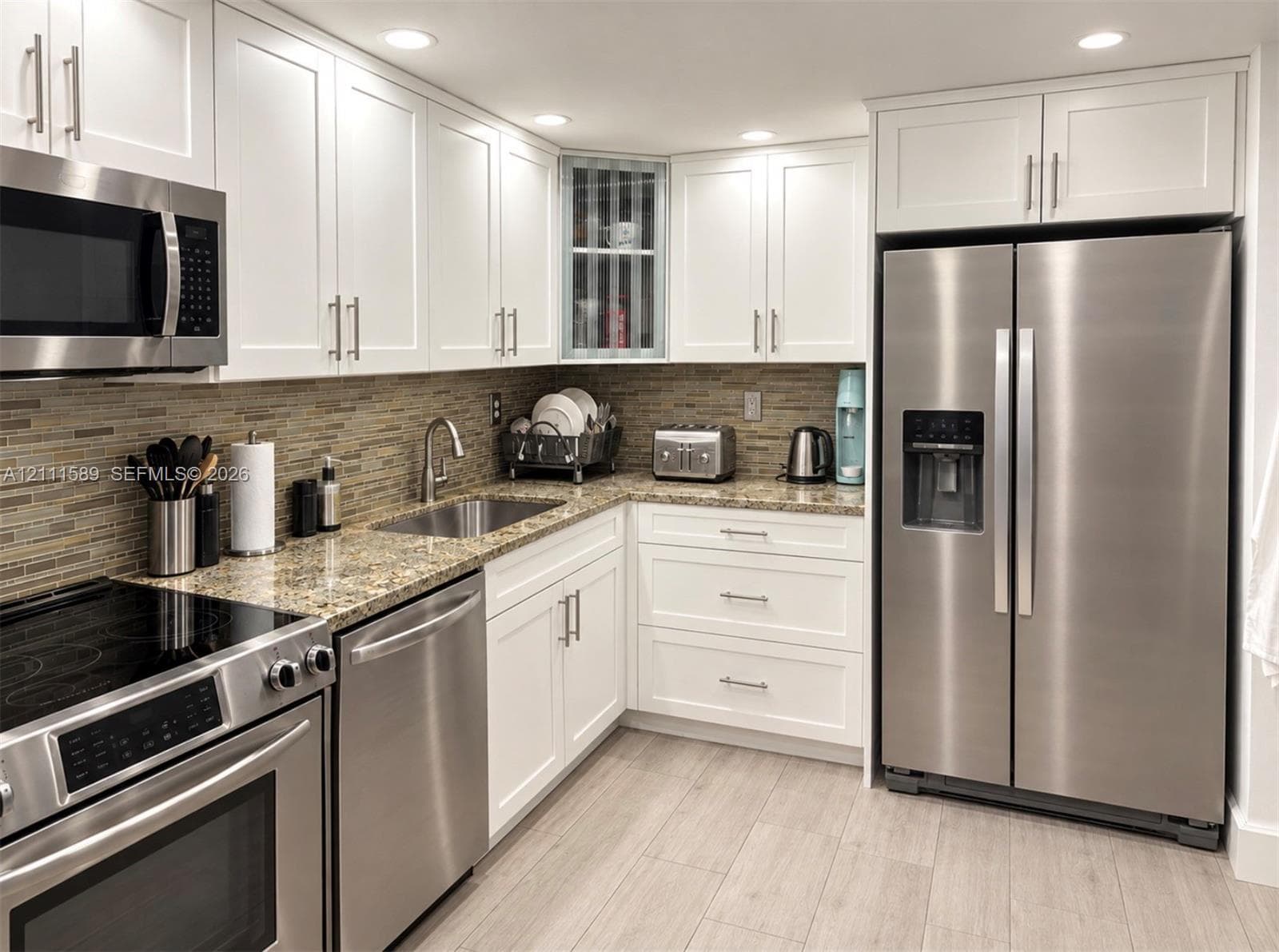 Kitchen featuring white shaker-style cabinetry, stainless steel appliances, stone-surface countertops, multi-toned tile backsplash, and wood-finish flooring