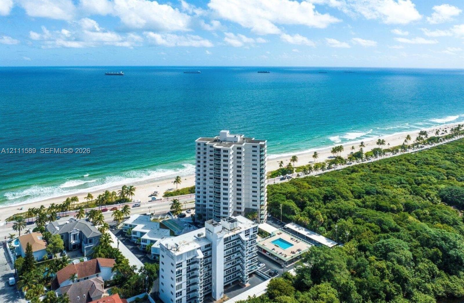 Aerial perspective of coastal high-rise buildings featuring a swimming pool, paved sundeck, and proximity to the shoreline