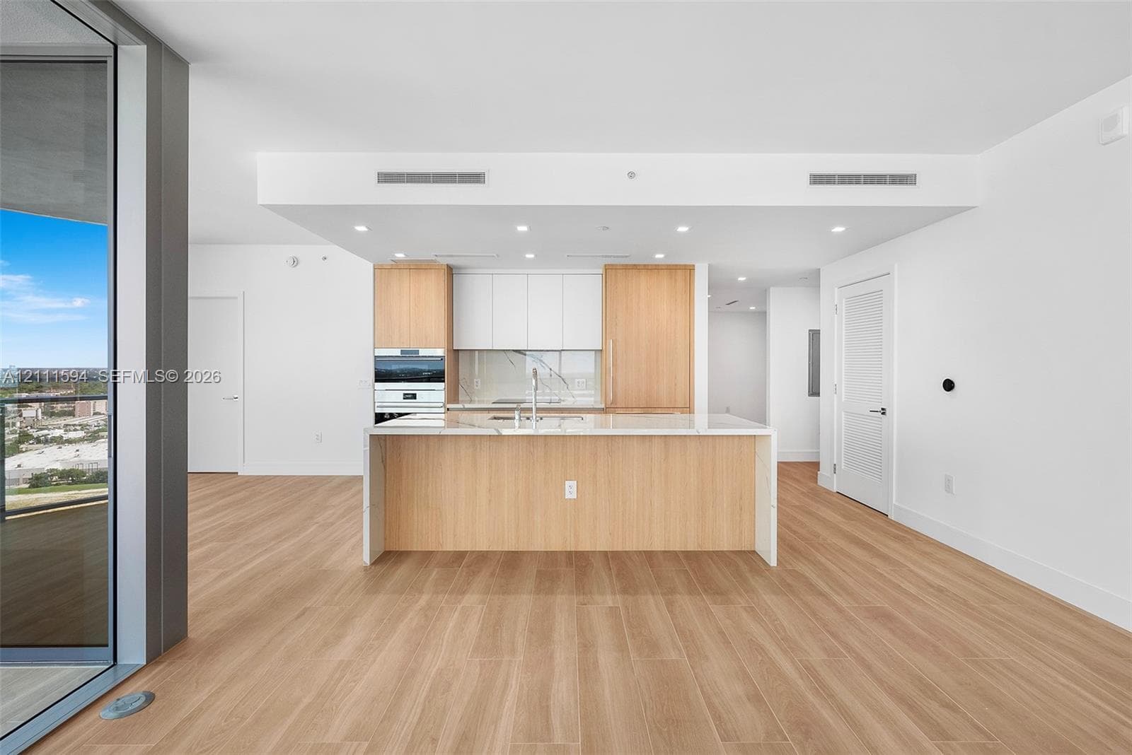 Kitchen featuring wood-finish cabinetry, white slab countertops, a central island, recessed lighting, and integrated wall oven