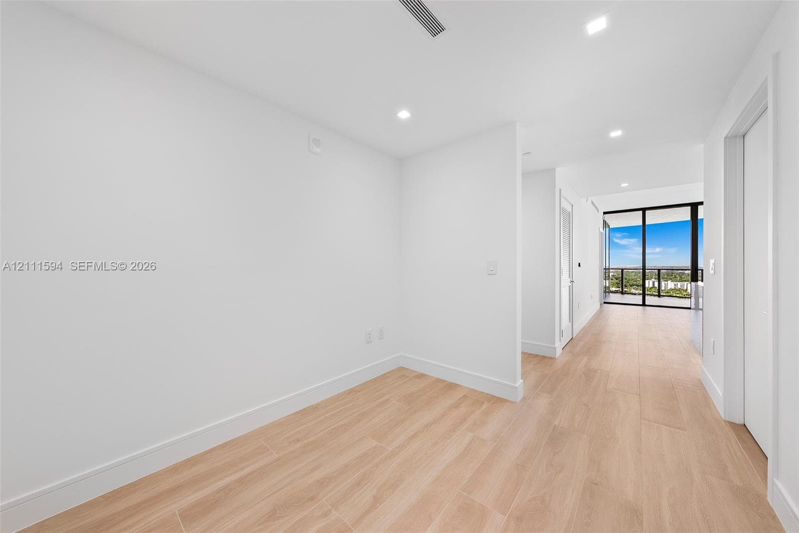 Interior space featuring light-toned wood-finish flooring, recessed ceiling lighting, and floor-to-ceiling glass sliding doors with balcony access