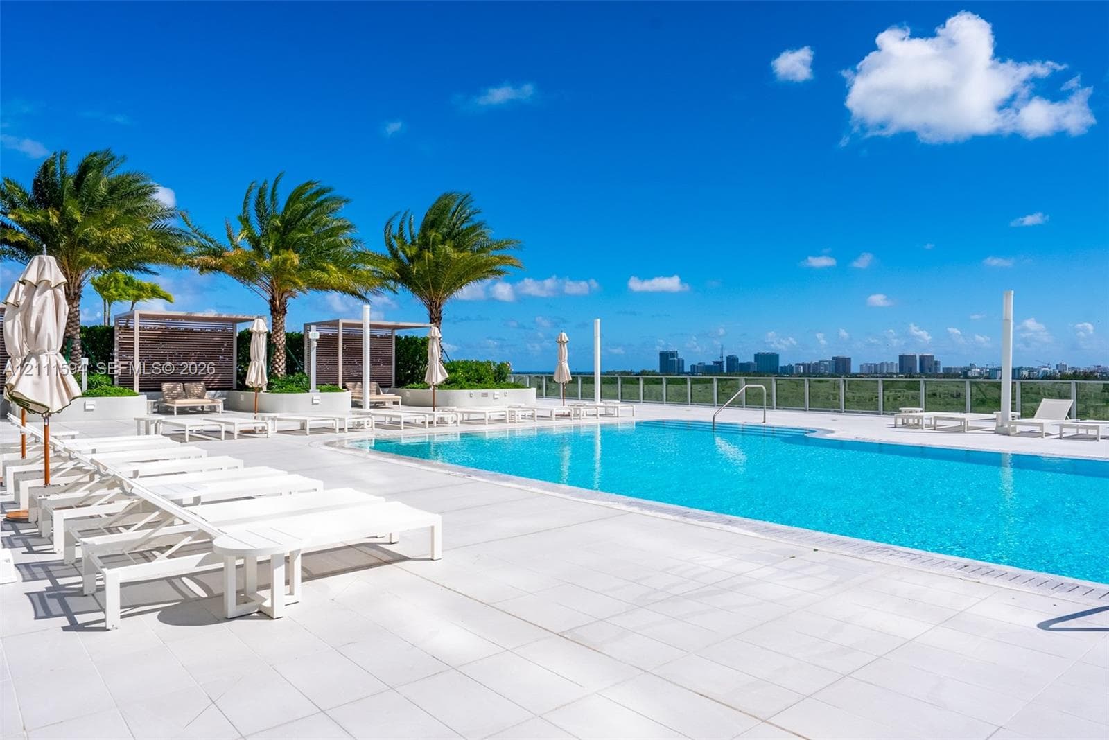 Rooftop pool deck featuring stone tile flooring, perimeter glass railings, built-in cabanas, and mature palm trees