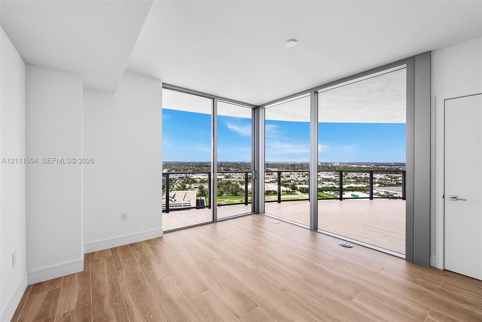 Floor-to-ceiling glass corner walls, wood-finish flooring, and expansive wrap-around balcony with metal railings