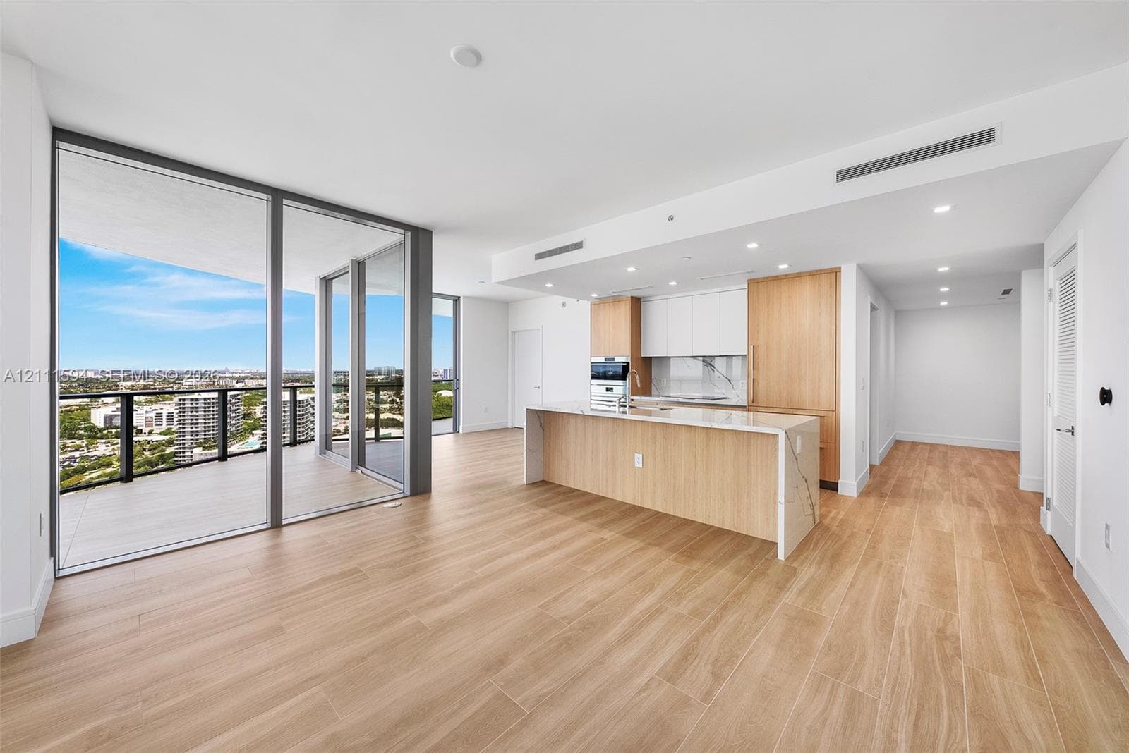 Open-concept interior featuring wood-finish flooring, floor-to-ceiling glass panel walls, a wraparound balcony, a kitchen island with stone-finish countertops, and minimalist flat-panel cabinetry