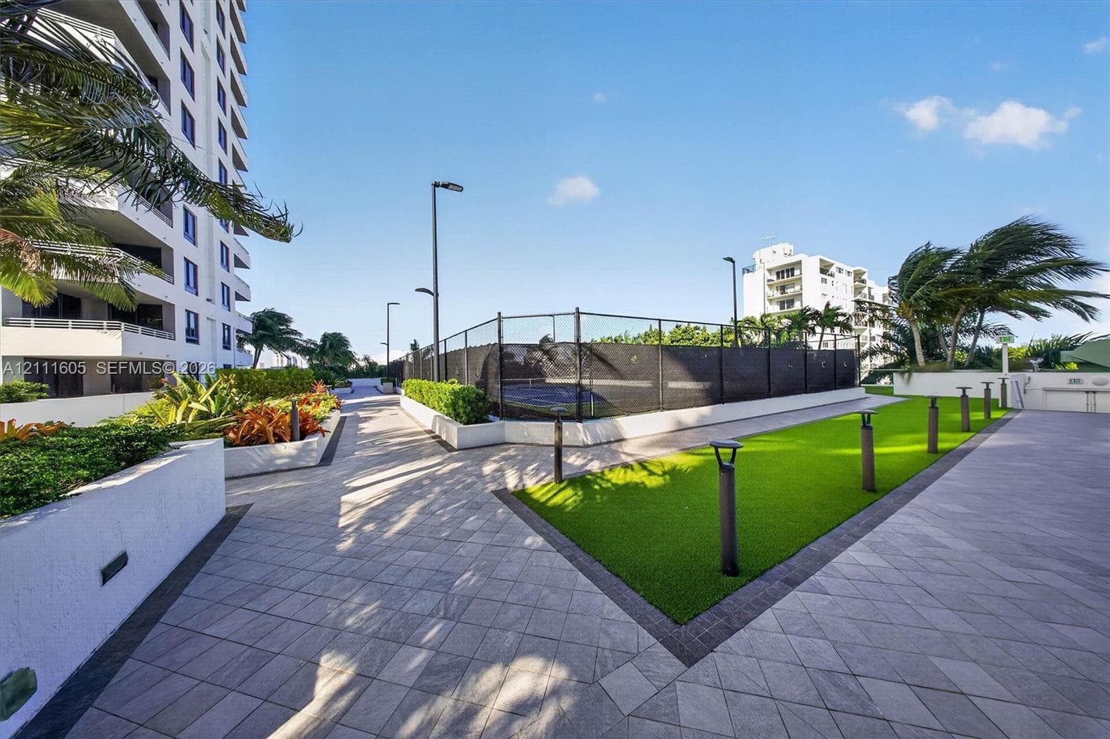 Recreational area featuring a fenced sports court, paved walkways, synthetic lawn, and landscaped planter boxes