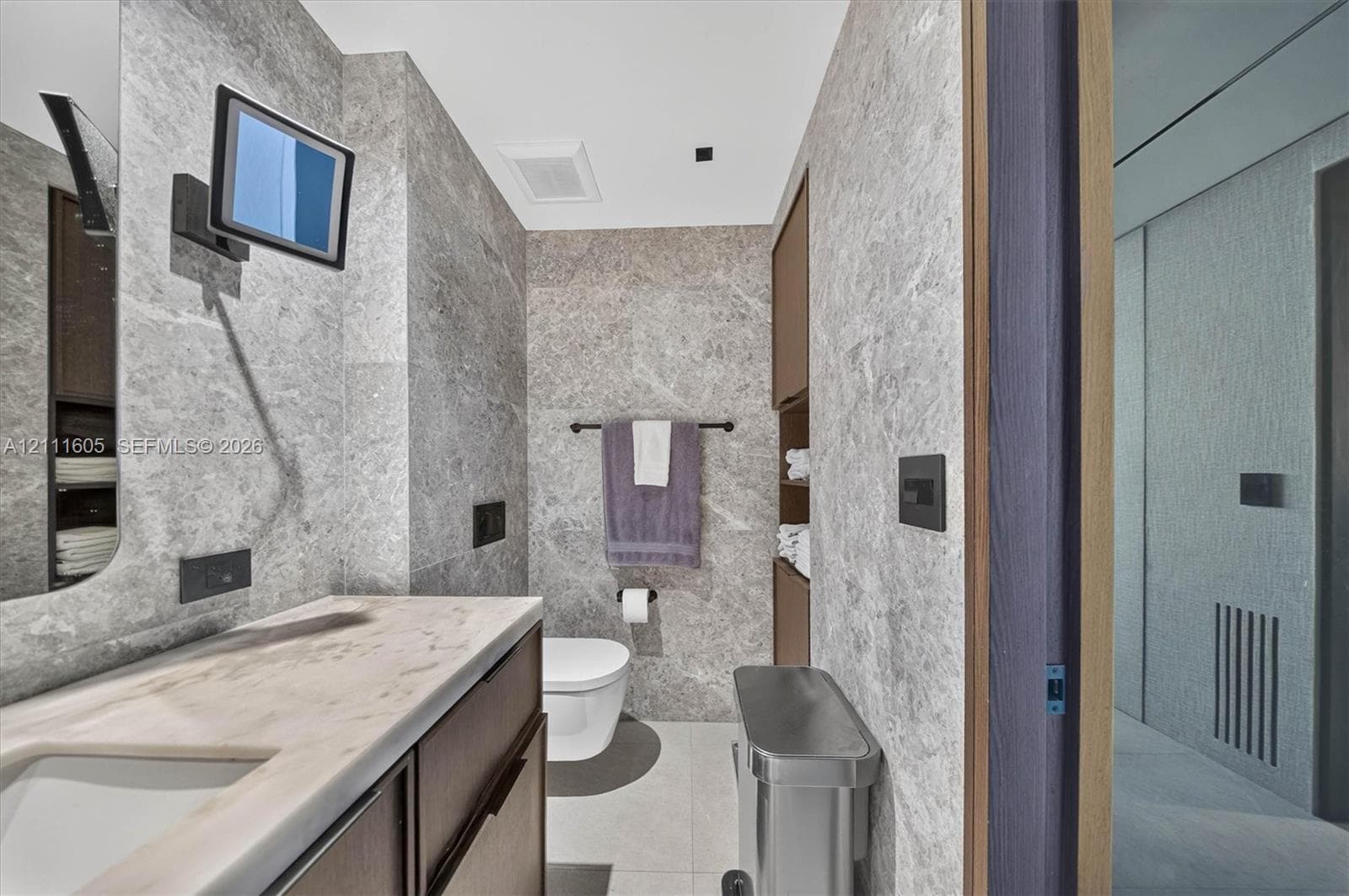 Full-height stone wall cladding, custom wood-finish vanity with an integrated basin, stone countertop, matte black hardware, and floor-to-ceiling built-in cabinetry