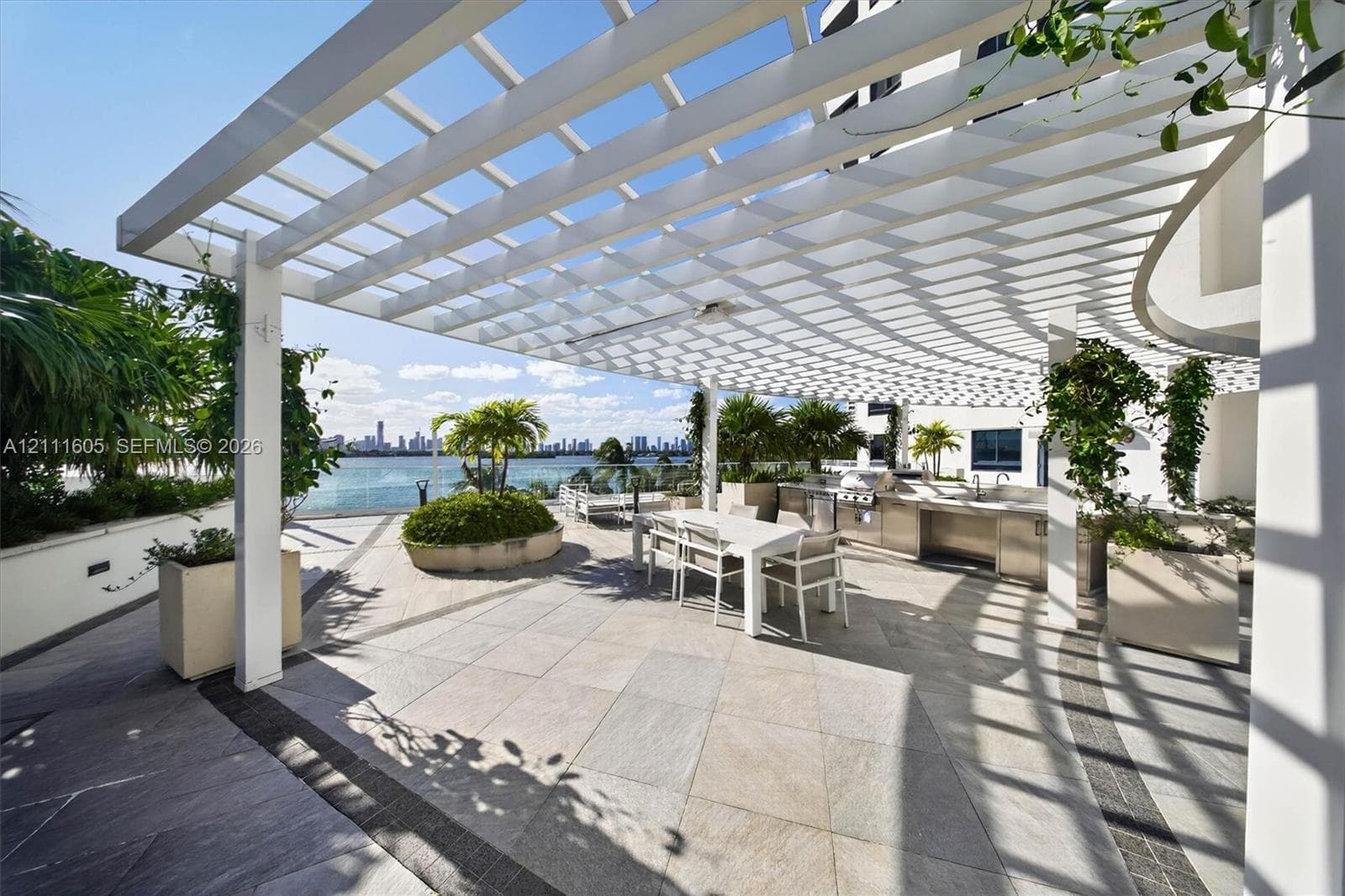 Expansive terrace featuring a large overhead pergola, built-in outdoor kitchen with stainless steel appliances, tile flooring, and integrated concrete planters
