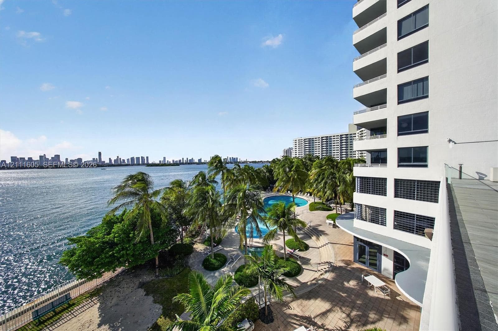 High-rise residential exterior with multi-level private balconies, waterfront swimming pool, manicured grounds featuring mature palm trees, and hardscaped patio areas