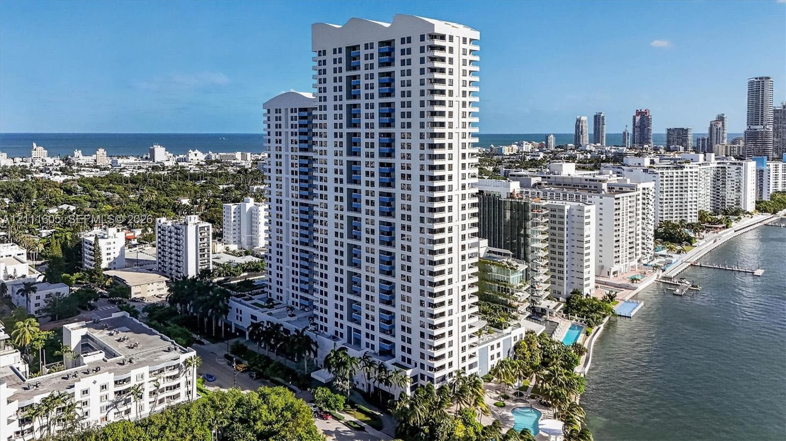 High-rise residential tower featuring a white facade, uniform balcony rows, blue-tinted glass, and an ground-level outdoor swimming pool