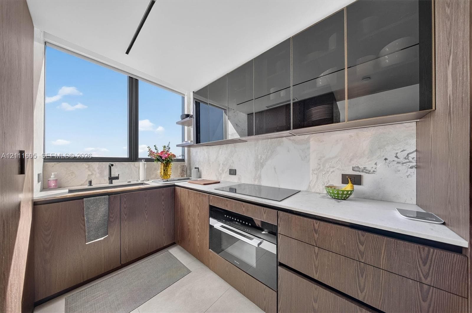 Kitchen featuring wood-finish cabinetry, stone-patterned backsplash, light-colored countertops, integrated cooktop and oven, and upper glass-front cabinets