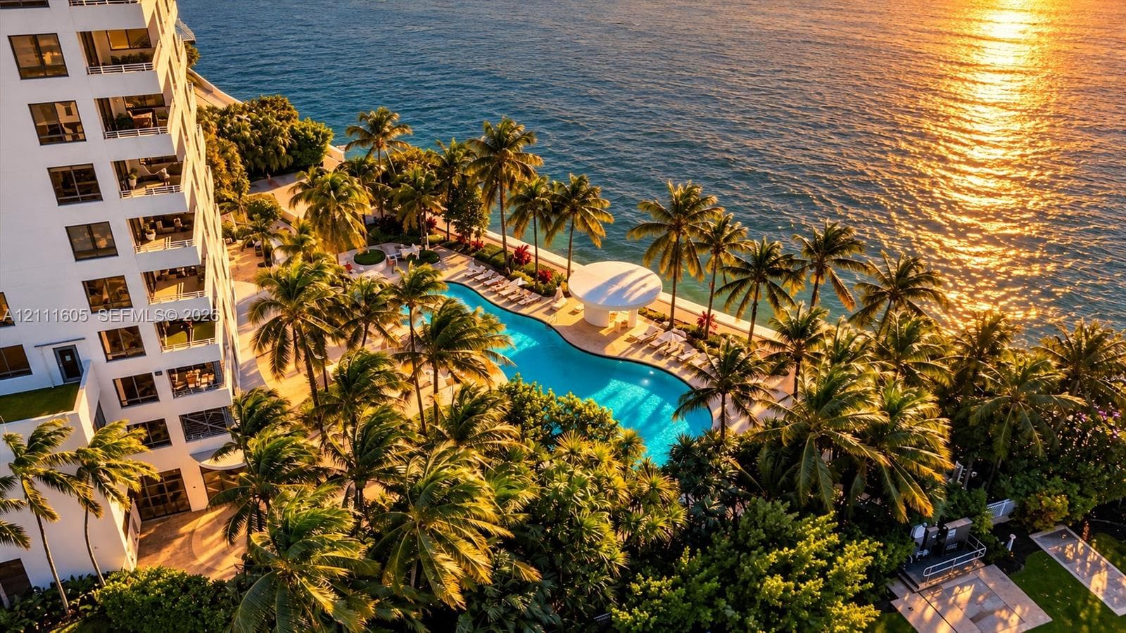 High-rise exterior featuring private balconies, a multi-level swimming pool, extensive palm tree landscaping, and direct access to the oceanfront