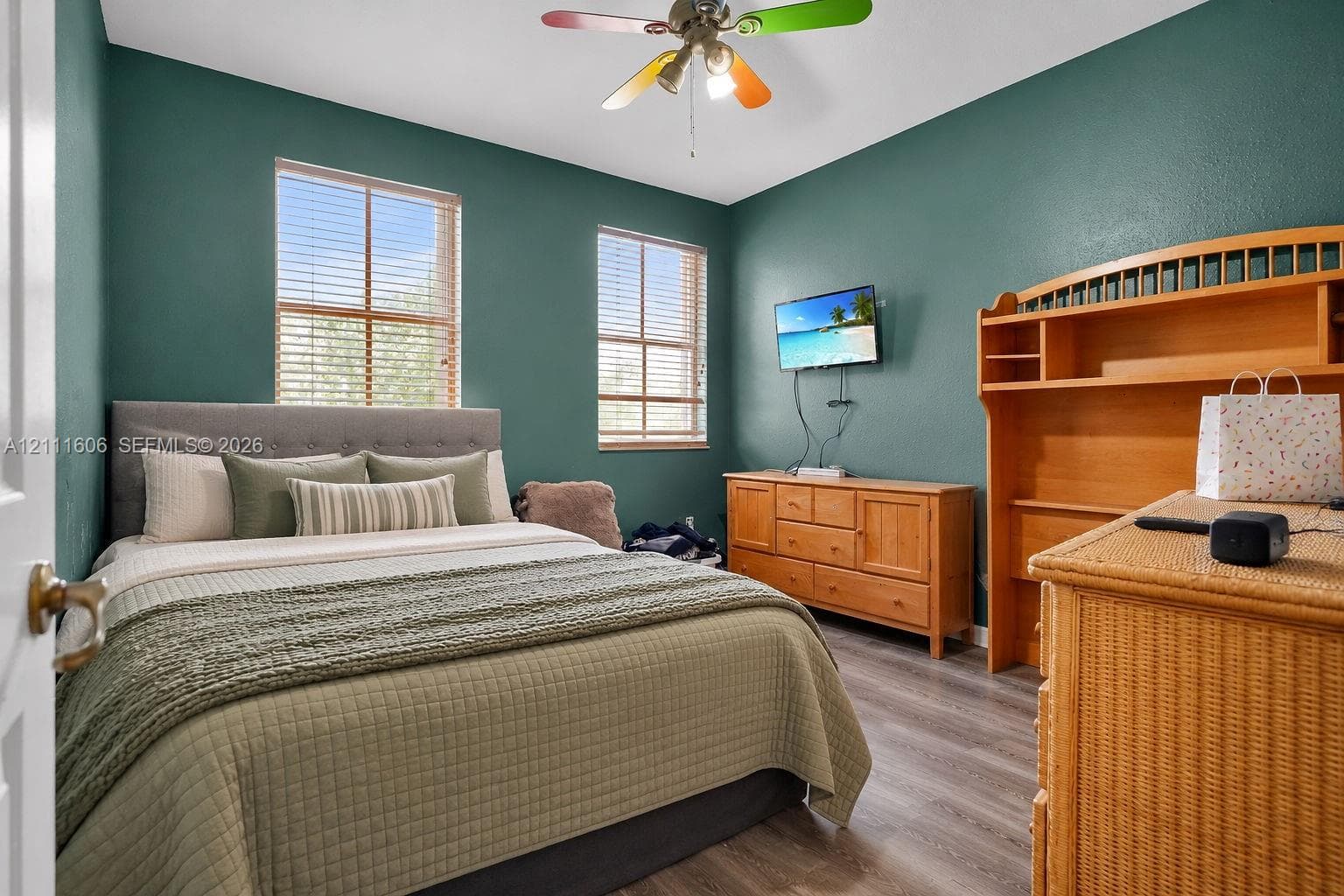 Room featuring wood-finish flooring, dual windows with horizontal blinds, and a multi-blade ceiling fan