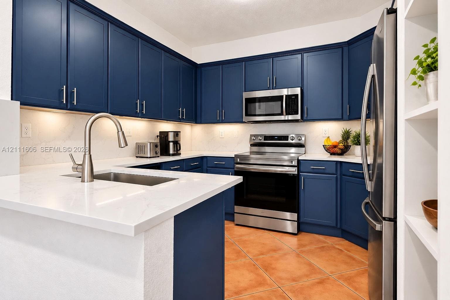 Kitchen featuring navy blue cabinetry, stainless steel appliances, light-toned stone-finish countertops, under-cabinet lighting, and ceramic tile flooring