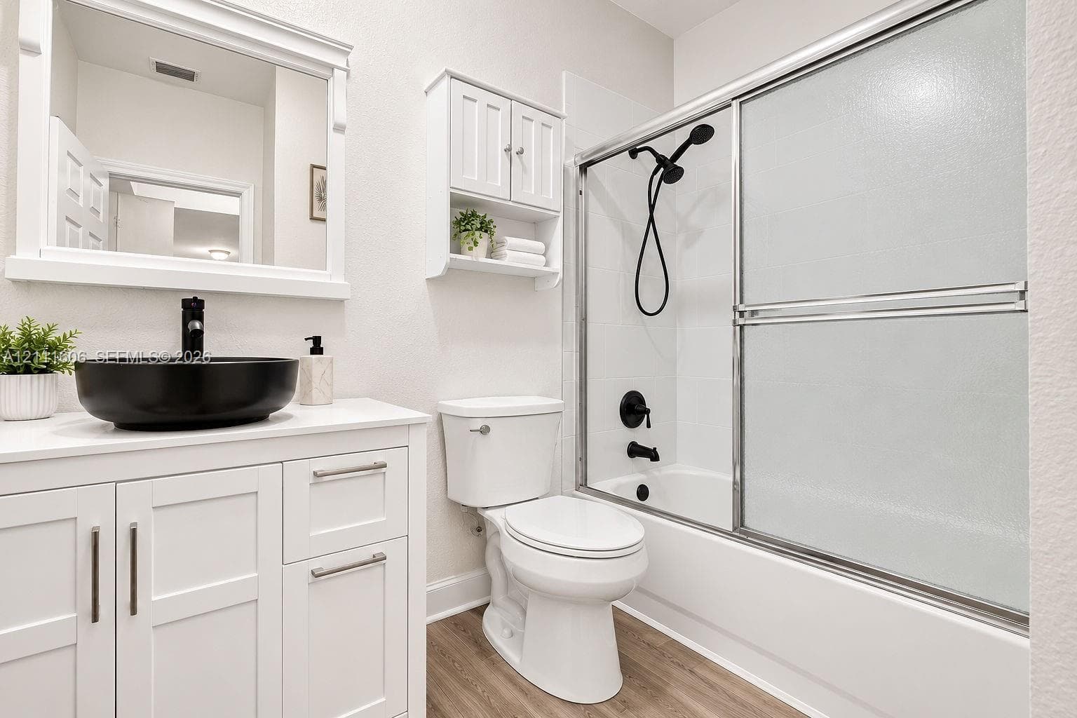 Bathroom featuring a white vanity cabinet with a vessel sink, quartz-style countertop, wall-mounted mirror, built-in medicine cabinet, and a shower-tub combination with matte black fixtures