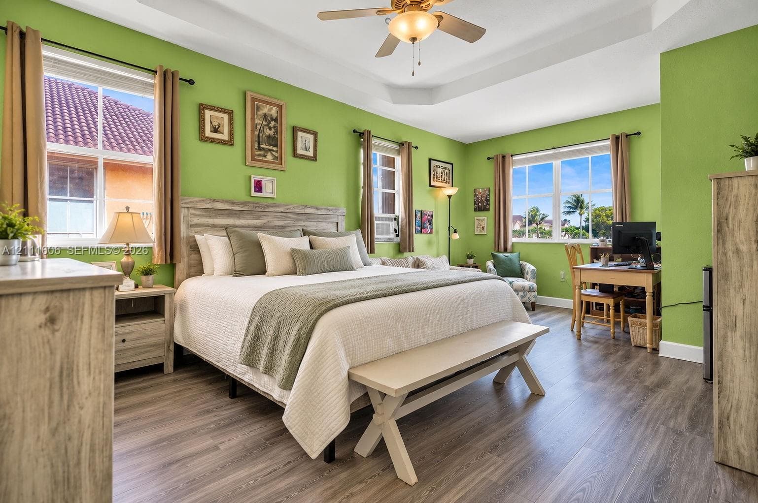 Tray ceiling featuring a central lighted ceiling fan, wood-finish flooring, and multiple large windows