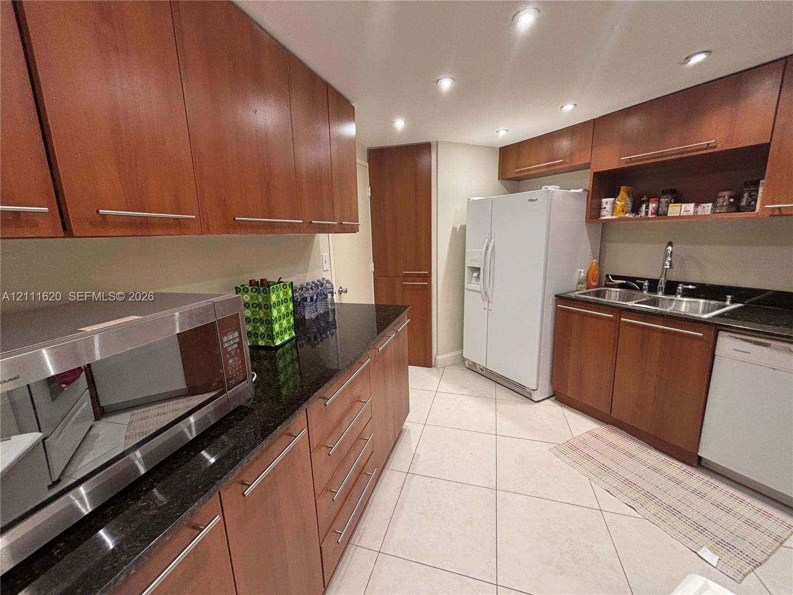 Kitchen featuring medium-tone wood cabinetry, dark stone countertops, recessed lighting, tile flooring, and integrated stainless steel and white appliances