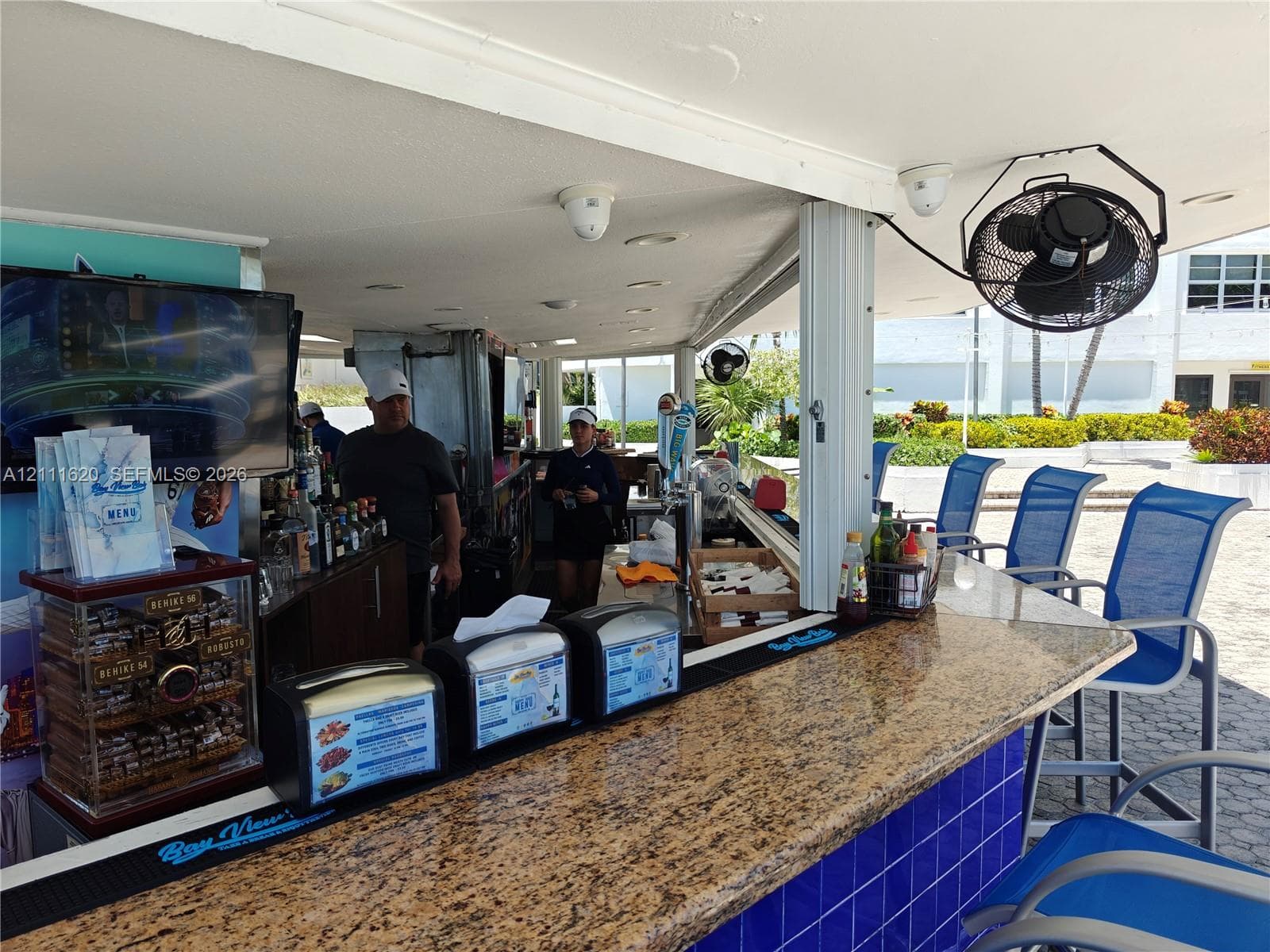 Covered outdoor bar area featuring a stone-surface countertop, vibrant blue tile base, recessed ceiling lighting, and wall-mounted industrial cooling fans