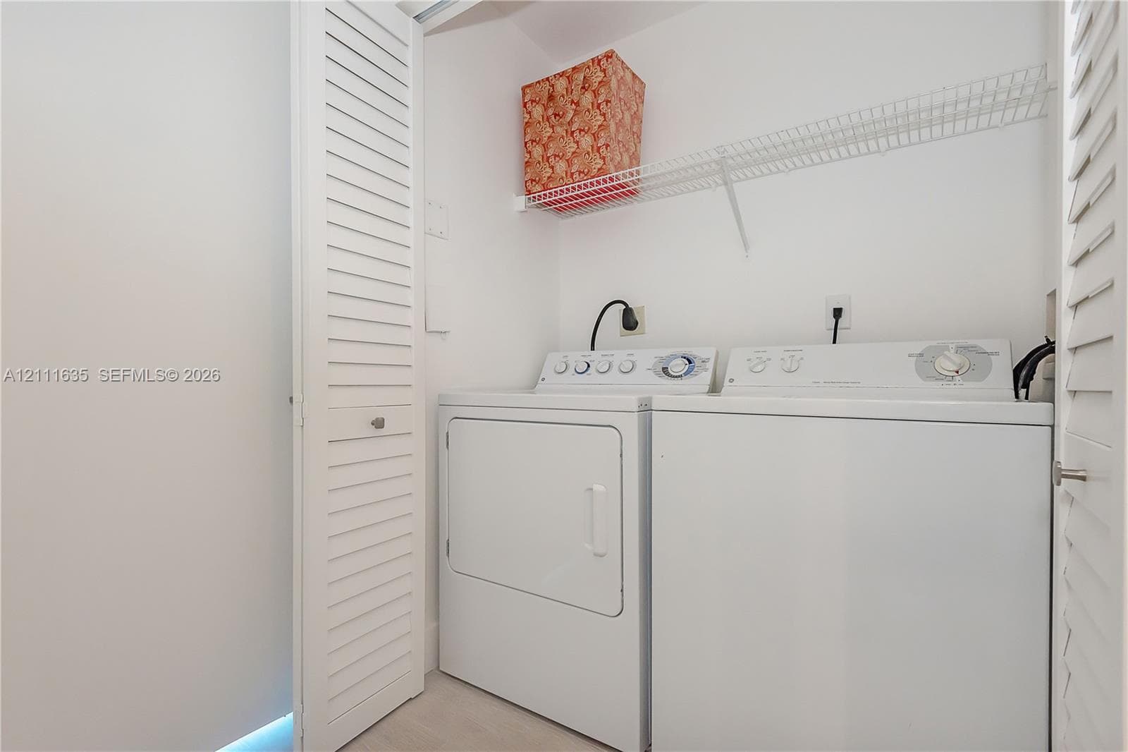 Laundry closet featuring white louvered doors, wire shelving, and dedicated hookups for a washer and dryer