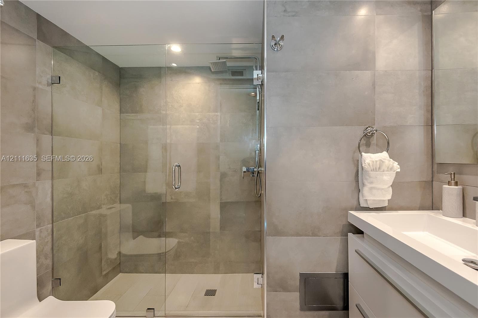 Walk-in glass-enclosed shower featuring large-format gray wall tiling, rainfall showerhead, floating vanity with integrated rectangular sink, and polished chrome fixtures