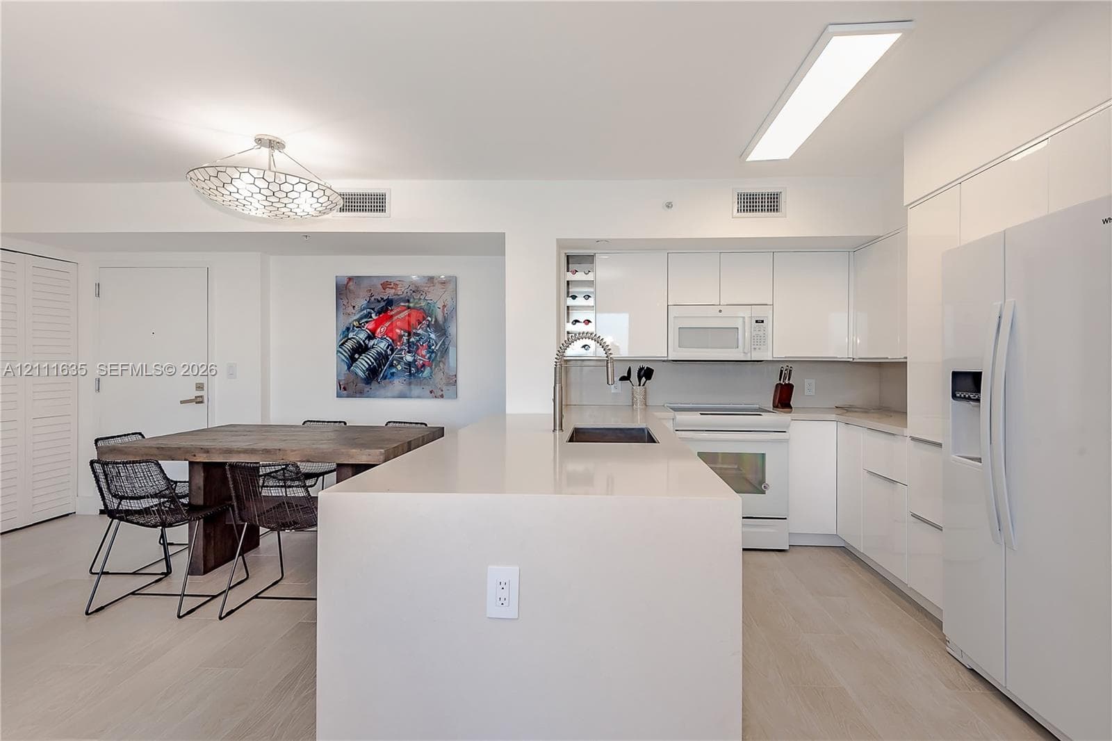 Kitchen featuring white slab cabinetry, an oversized quartz waterfall island, built-in wine storage, light-toned wood-finish flooring, and a modern geometric pendant light fixture