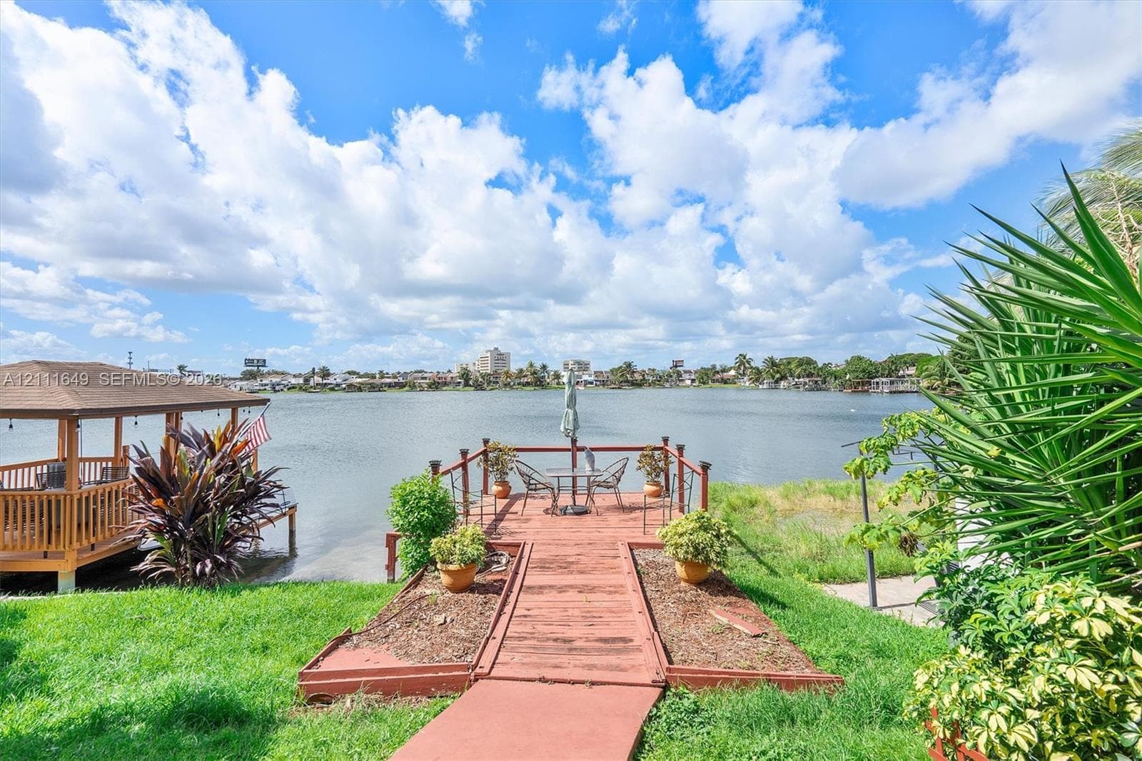 Waterfront property featuring a wooden gazebo, a deck extending over the water, and mature landscaping
