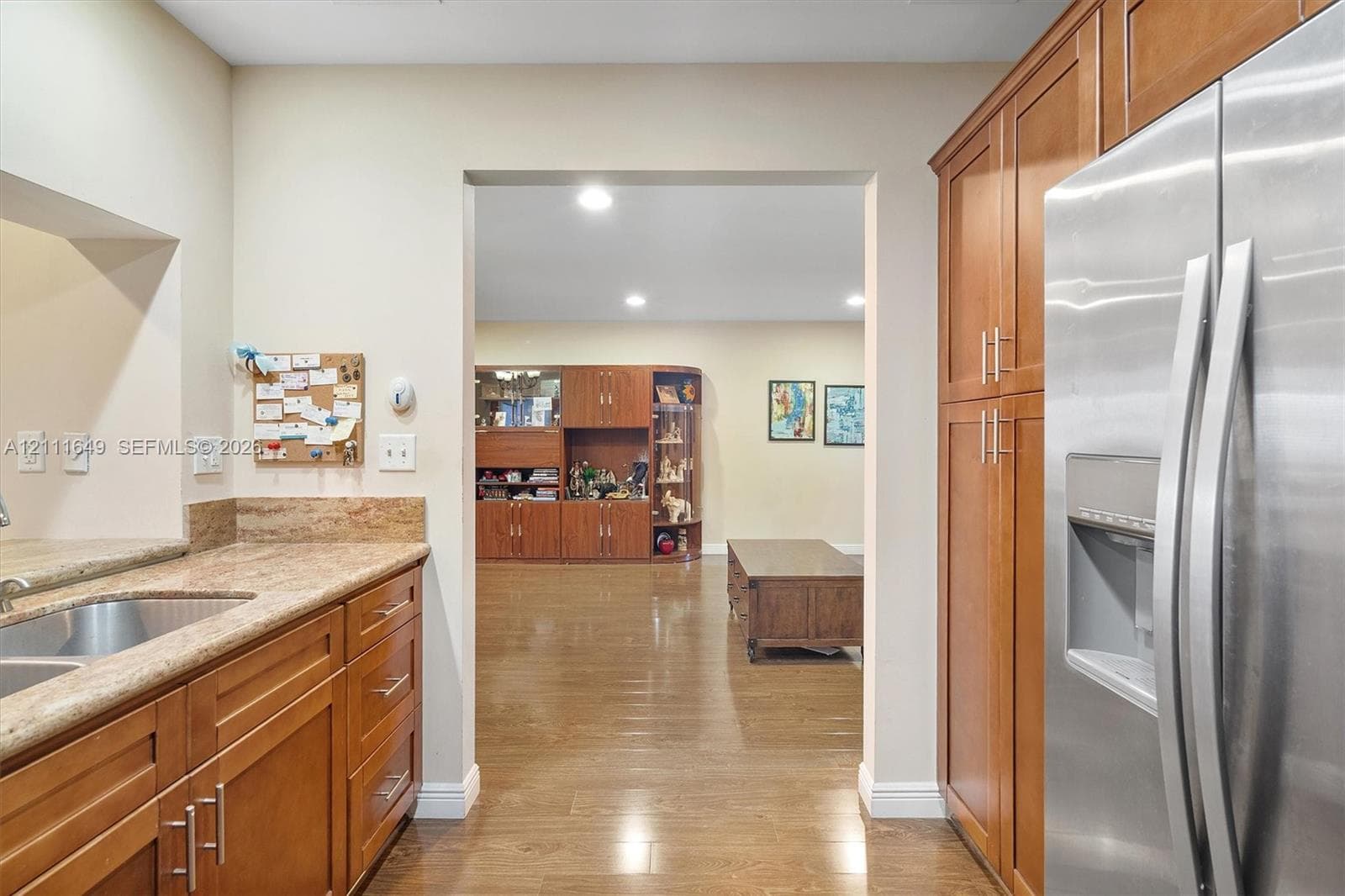 Kitchen featuring wood cabinetry, stone countertops, stainless steel refrigerator, undermount sink, and recessed lighting