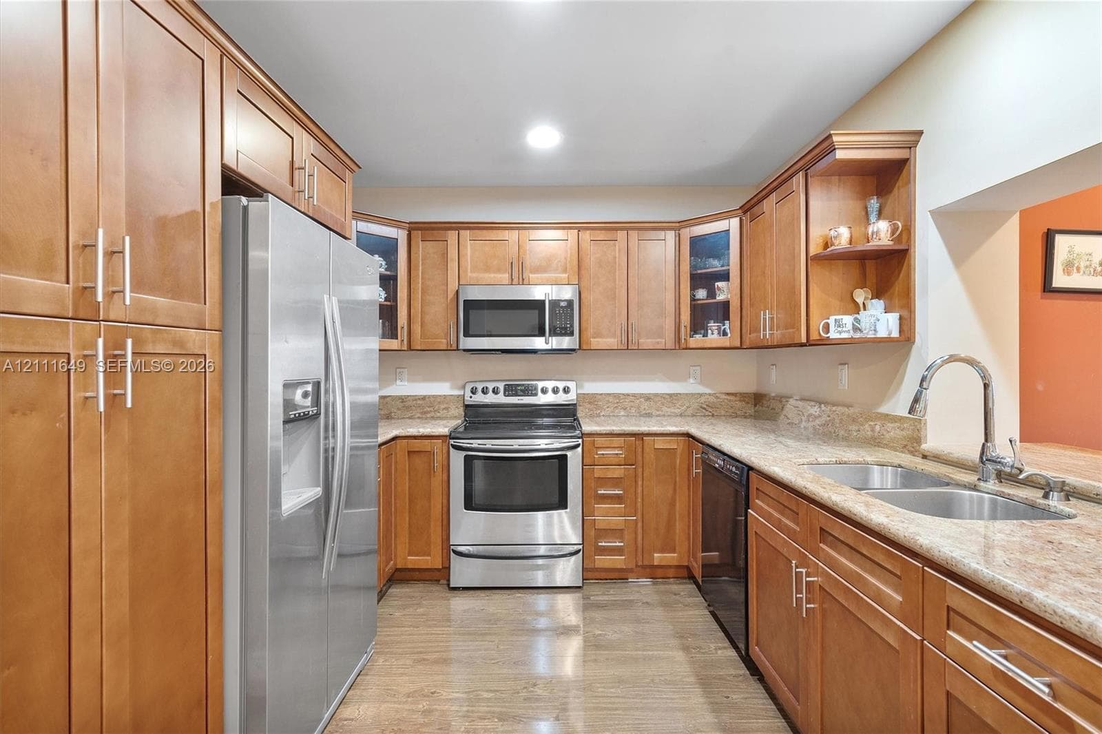 Kitchen featuring warm-tone cabinetry, stone-finish countertops, stainless steel appliances, glass-front upper cabinet doors, and wood-finish flooring