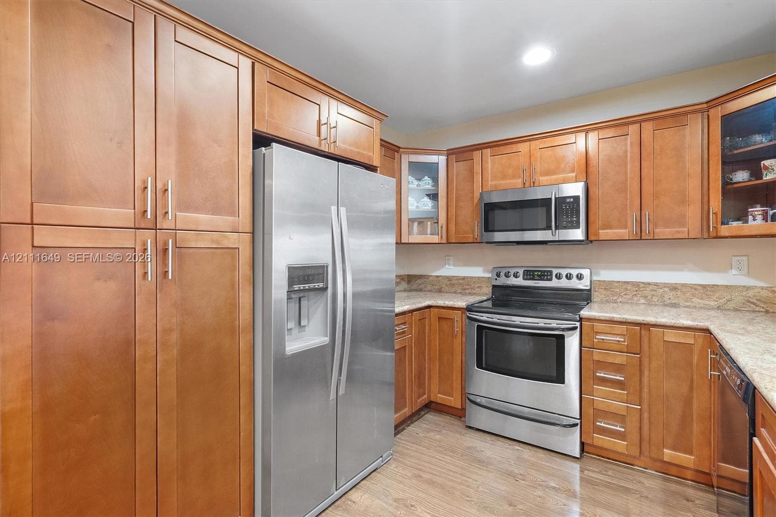 Kitchen featuring medium-tone wood cabinetry, stone countertops, stainless steel appliances, and wood-finish flooring